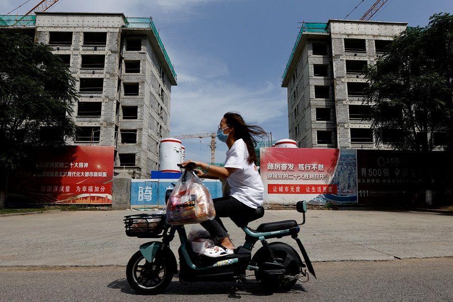 A person rides a scooter past a construction site of residential buildings in Tianjin, China, on 18 August 2023. (Tingshu Wang/Reuters)