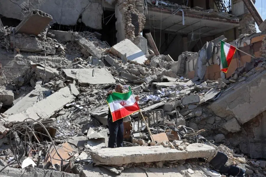 A man holds an Iranian flag amid the debris of a destroyed building following airstrikes in central Tehran on 4 March 2026.