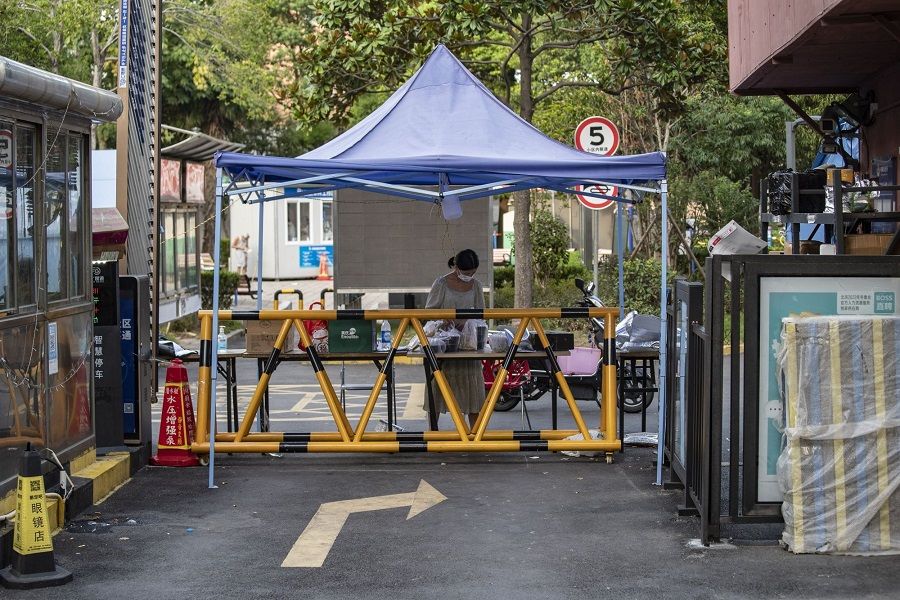 A woman collects her deliveries at the barricaded entrance of a residential complex as several city blocks are sealed off due to Covid-19 in the Meilong township of Shanghai, China, on 15 August 2022. (Qilai Shen/Bloomberg)