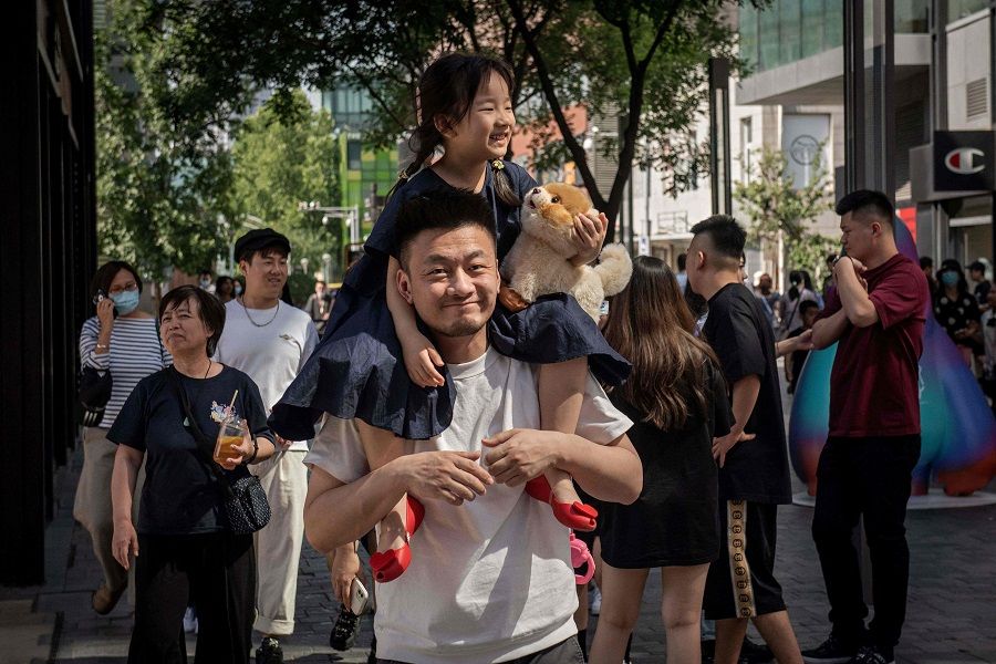 A young girl sits on her father's shoulders outside a shopping mall in Beijing, China, on 1 June 2021. (Nicolas Asfouri/AFP)