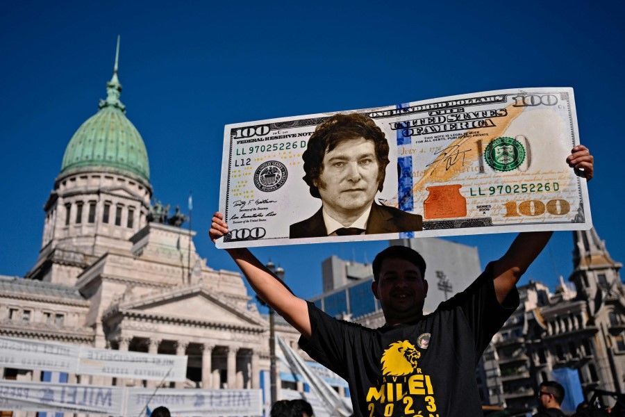 A supporter of Argentina's President-elect Javier Milei displays a one hundred dollar bill placard with an image of the future president as he waits outside the Congress before his inauguration ceremony, in Buenos Aires on 10 December 2023. Argentina's President Javier Milei marks 100 days in office on 19 March 2024. (Luis Robayo/AFP)