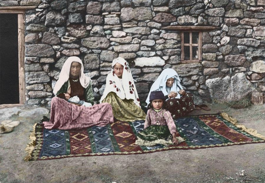 The Crimean peninsula, 1890s. A carpet lies outside a home, with a few Tatar womenfolk sitting cross-legged. They are wearing blouses and long skirts, with their heads wrapped in decorative headdresses. The Crimea was once home to the Mongolian Golden Horde (Ulug Ulus, "Great State" in Turkic), so the Tartars of Eastern origin are one of the major ethnic groups today.