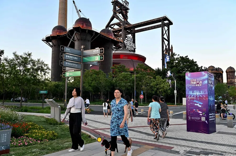 People walk past a steel mill-turned-urban area at an industrial heritage site in the Shougang park of Beijing on 17 July 2024.  (Adek Berry/AFP)