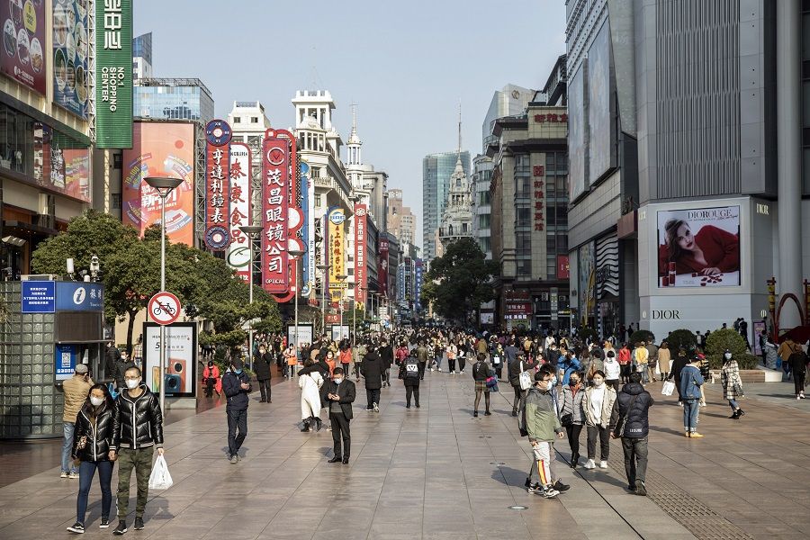 Shoppers and pedestrians wearing protective masks walk past stores on Nanjing Road in Shanghai, China, on 14 March 2020 as China returns to work slowly. (Qilai Shen/Bloomberg)