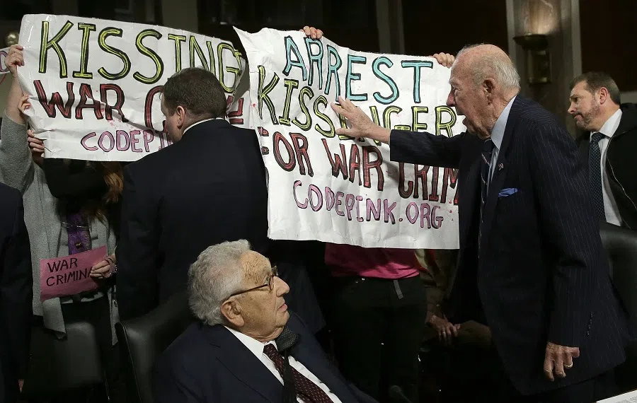 Former US Secretary of State George Shultz (right) pushes away protesters shouting "Arrest Henry Kissinger for war crimes" as former US Secretary of State Henry Kissinger (left) watches prior to the two testifying before the Senate Armed Services Committee 29 January 2015 in Washington, DC. (Win McNamee/Getty Images North America/AFP)
