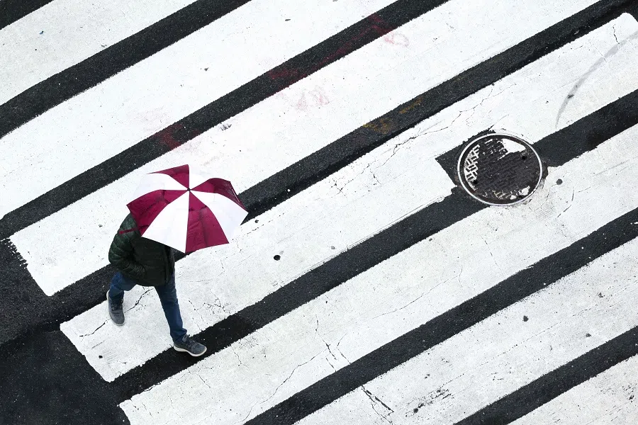A person holds an umbrella while walking across a street as it rains in the Manhattan borough of New York City on 24 March 2025.