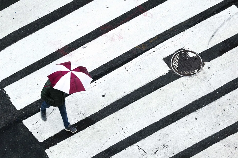 A person holds an umbrella while walking across a street as it rains in the Manhattan borough of New York City on 24 March 2025. (Charly Triballeau/AFP)