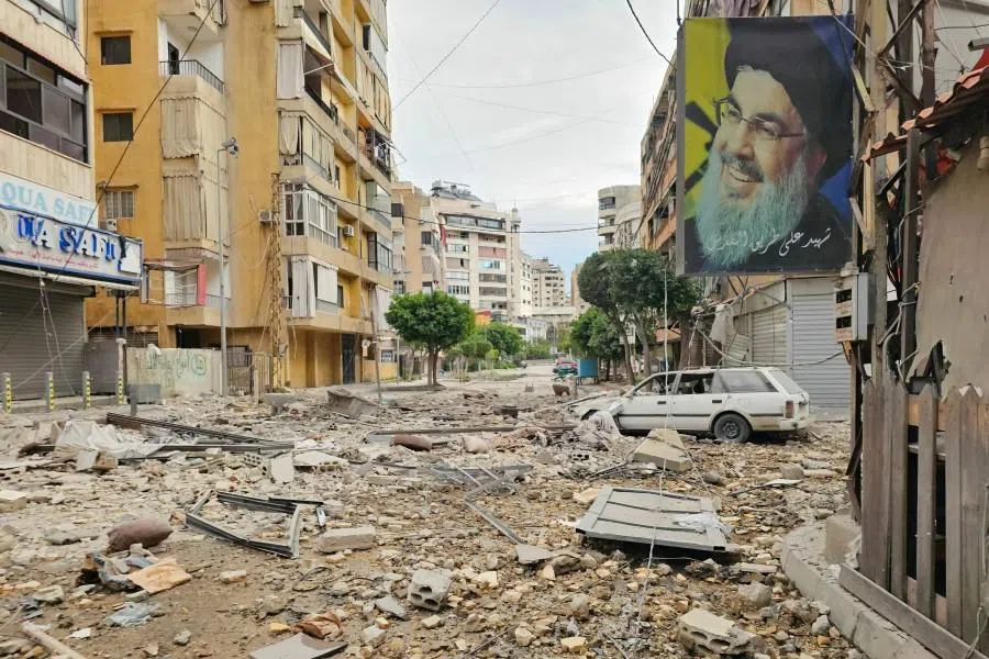 A banner bearing the image of Hassan Nasrallah, the assassinated leader of the Lebanese Shia movement Hezbollah, hangs from a building along a street littered with building debris at the site of an overnight Israeli airstrike that targeted a neighborhood in Beirut’s southern suburbs on 25 March 2026. (AFP)