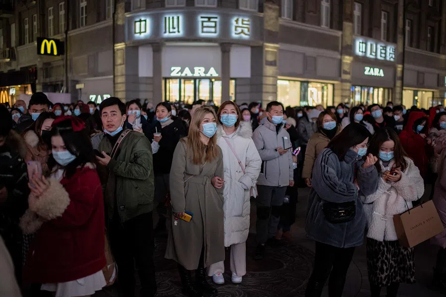 People wearing face masks stand around a giant 3D screen on Jianghan street in Wuhan on 10 January 202. (Nicolas Asfouri/AFP)