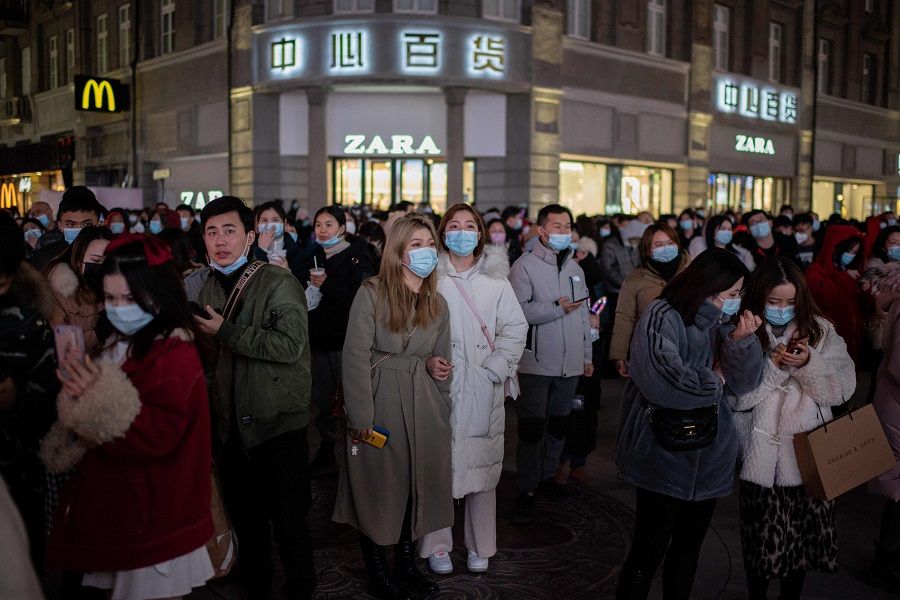People wearing face masks stand around a giant 3D screen on Jianghan street in Wuhan on 10 January 202. (Nicolas Asfouri/AFP)
