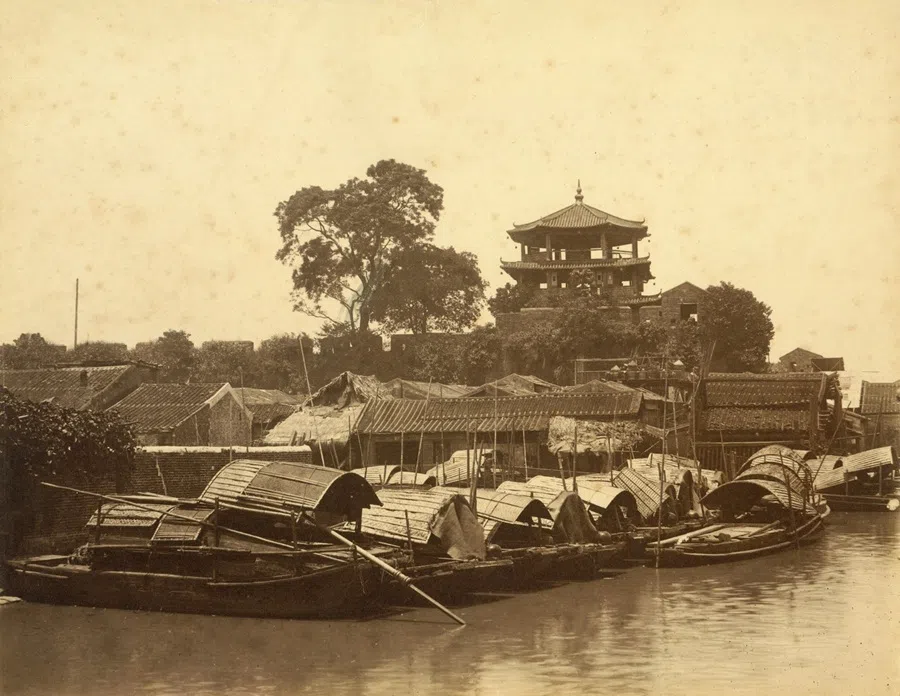 Guangzhou’s ancient city walls in the 1880s, built along the river, with boats moored nearby, presenting an evocative scene from an earlier age.