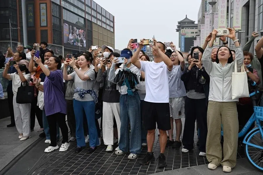 People take photos as US President Donald Trump’s motorcade passes the Wangfujing shopping street on the way to the airport after Trump met with Chinas President Xi Jinping in Beijing on 15 May 2026.