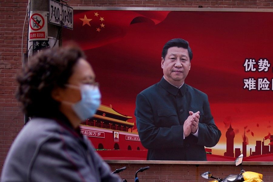 A woman walks past a portrait of Chinese President Xi Jinping on a street in Shanghai, 12 March 2020. (Aly Song/REUTERS)