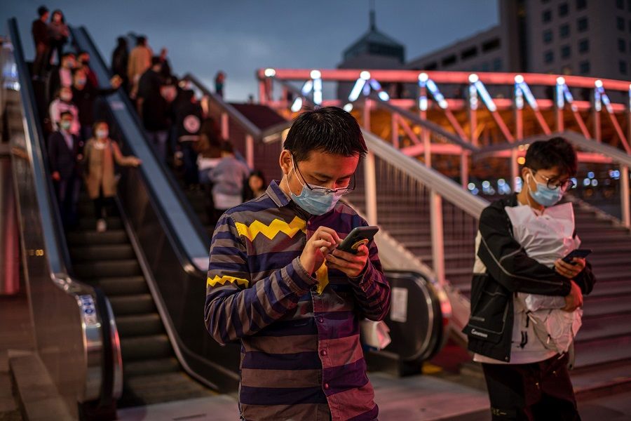 Mask-clad people are seen using their phones outside a shopping mall in Beijing on 11 October 2020. (Nicolas Asfouri/AFP)