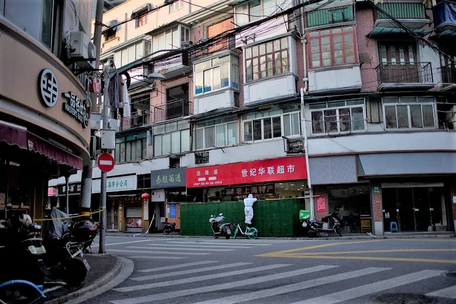 A woman in a protective suit tries to buy goods from a shop behind barricades of a sealed-off area during lockdown, amid the Covid-19 pandemic, in Shanghai, China, 4 May 2022. (Aly Song/Reuters)