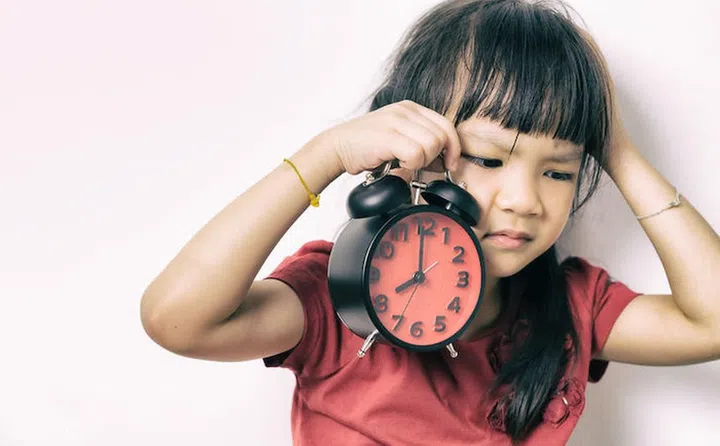 68402875 - little asian girl is angry at the alarm clock for waking her up. a kid in red shirt is upset that the alarm clock wake up her so early. lazy japanese girl doesn't want to get up in the morning.