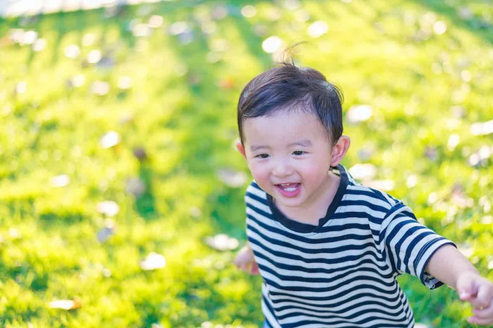 Little Asian kid playing and smiling at the playground under the sunlight in summer, Kids play on school yard. Happy kid in kindergarten or preschool. shallow DOF