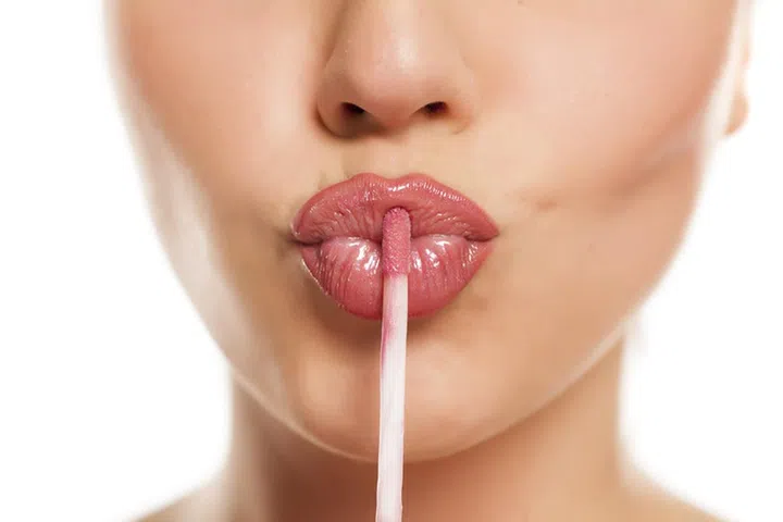young beautiful woman apply a lip gloss on her lips on white background