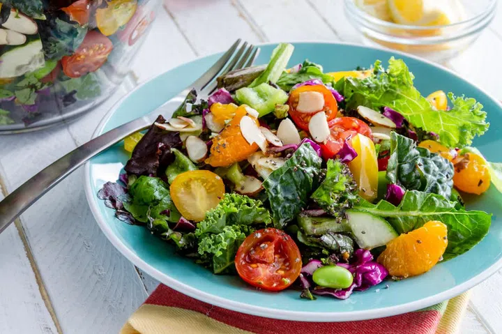 Fresh organic super food salad sitting on blue plate with fork on side