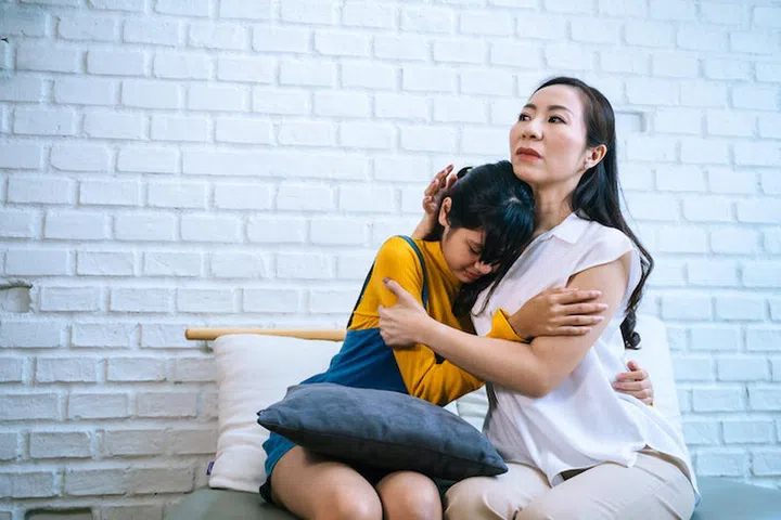 Asian mother comforting crying teenage daughter in miserable, stressed, depressed, sad state of mind. 40s Mom is hugging this adolescent teenager shoulders at indoors room.