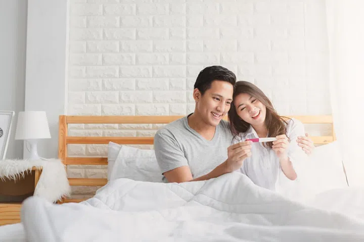 Happy Asian couple smiling after find out positive pregnancy test in bedroom at home