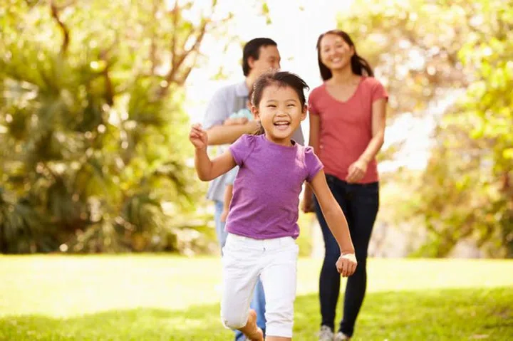 Family With Baby In Carrier Walking Through Park