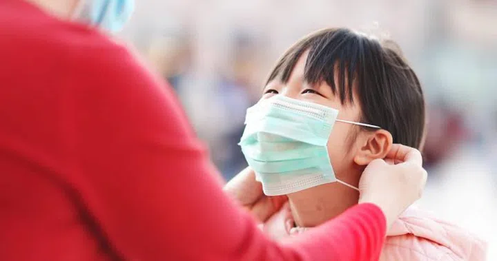 Asian mom helps her little daughter wear face mask