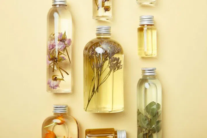 top view of transparent bottles with natural beauty products and dried wildflowers on yellow background