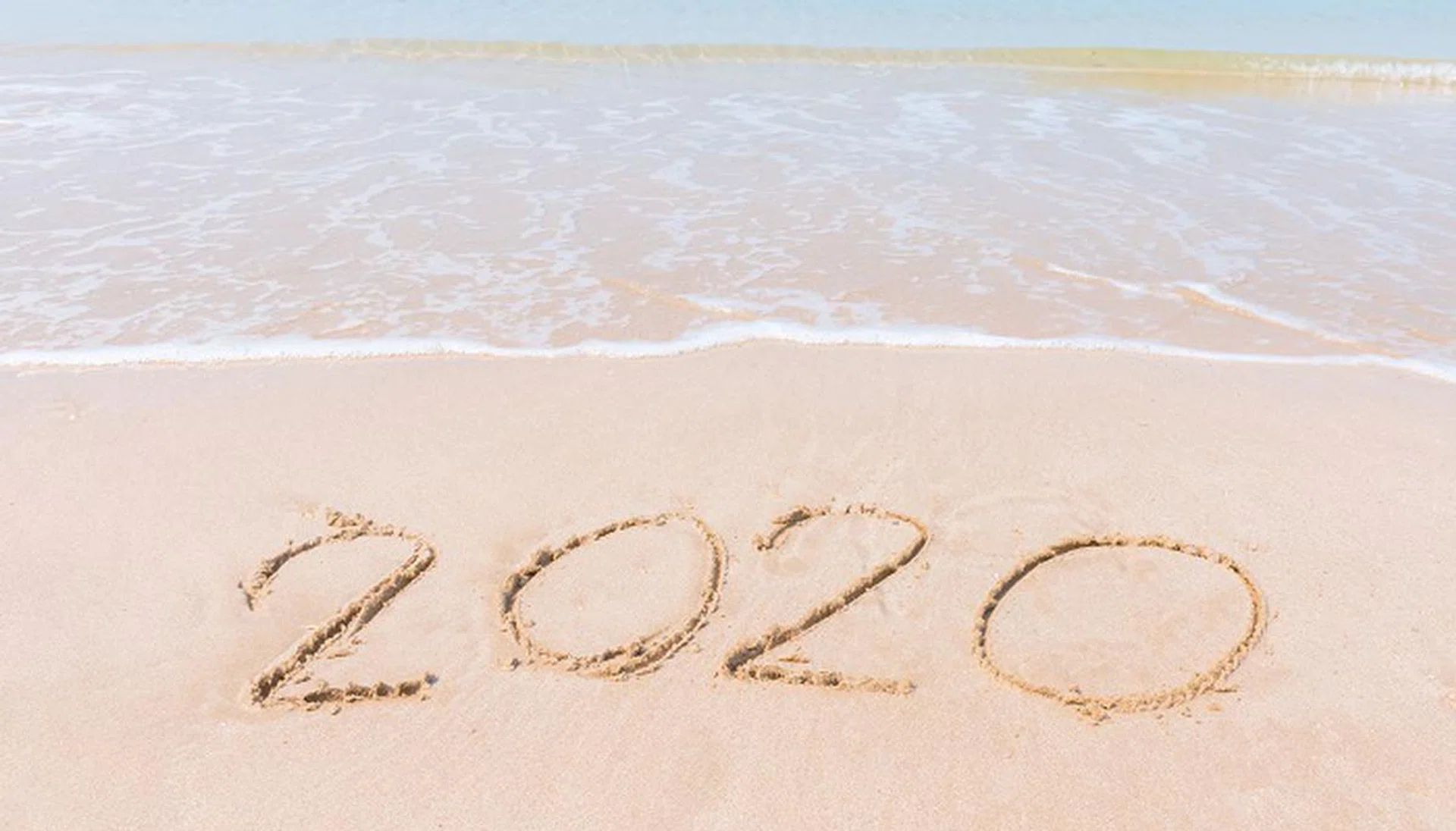 number handwritten 2020 on sandy beach with soft ocean wave on background