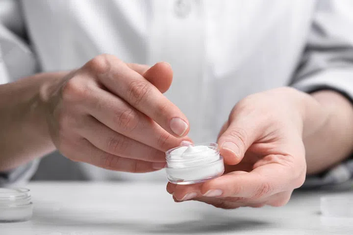 Woman with cream at table in cosmetic laboratory, closeup