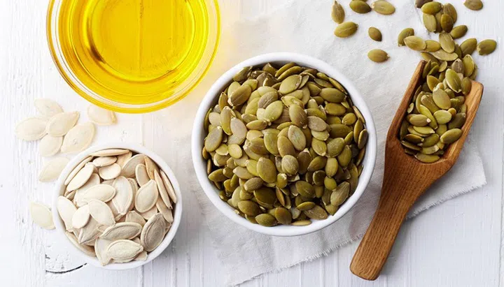 Bowl of pumpkin seed oil and pumpkin seeds on white wooden background. From top view