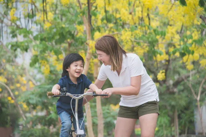 Beautiful and happy Asian mother teaching her cute son to ride a bicycle