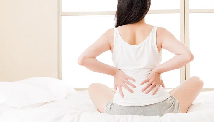 66729439 - asian woman suffers from back pain backache, spinal or lower back problem. bedroom background