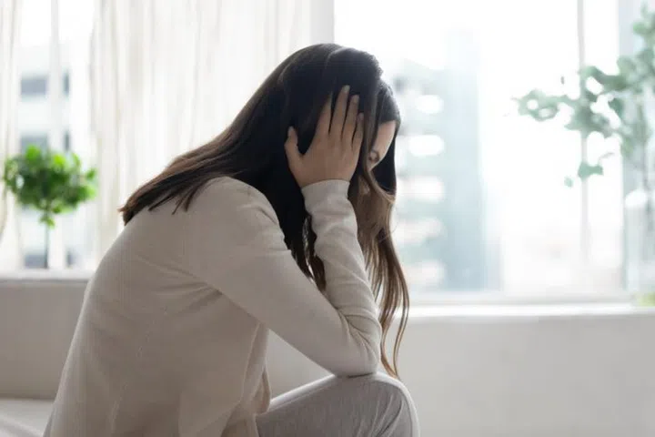Unhappy depressed woman sitting on couch alone, thinking about problems, touching temples, frustrated upset girl suffering from break up with boyfriend or divorce, unexpected pregnancy