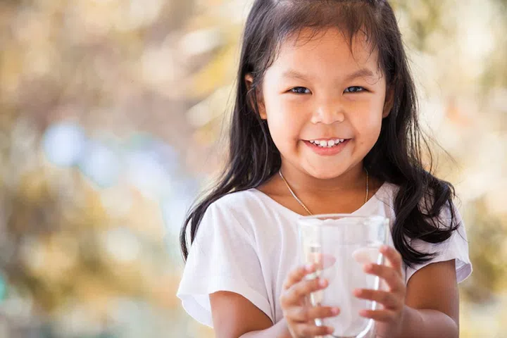 Cute asian little girl holding glass of fresh water in vintage color tone