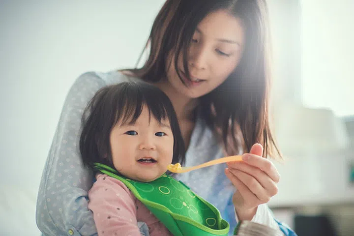 Pretty japanese woman feeding her baby daughter with spoon