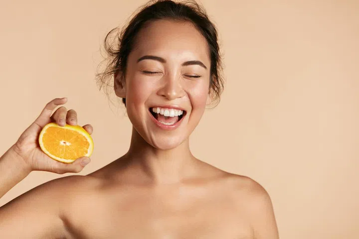 Beauty. Smiling woman with radiant face skin and orange portrait. Beautiful smiling asian girl model with natural makeup, healthy smile and glowing hydrated facial skin. Vitamin C cosmetics concept (Beauty. Smiling woman with radiant face skin and ora