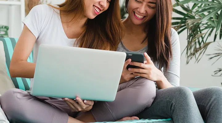Beautiful young asian women LGBT lesbian happy couple sitting on sofa buying online using laptop a computer and phone in living room at home. LGBT lesbian couple together indoors concept.