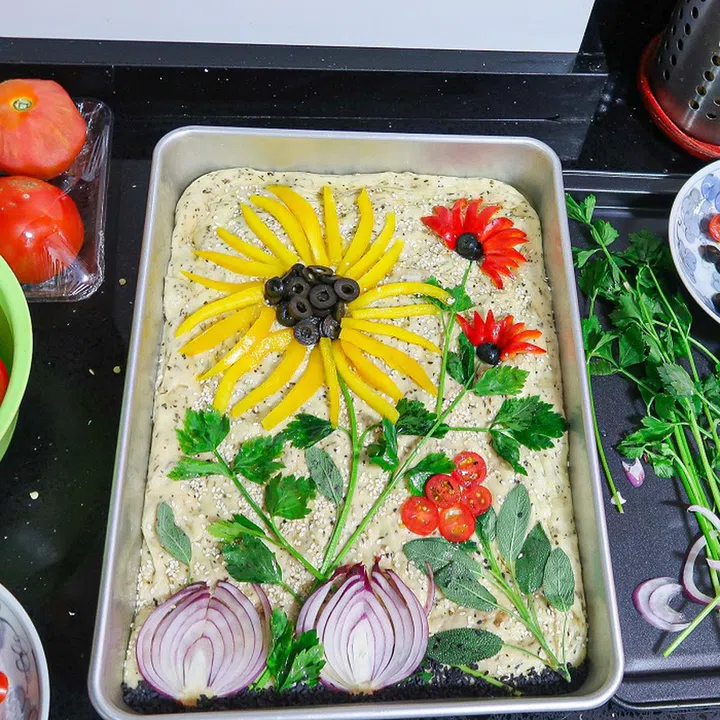 Now, let’s get artsy! Decorate the top of the dough with your sliced vegetables. Once you are happy with your artwork, finish off by gently brushing everything with olive oil to ensure that the vegetables and leaves don’t burn in the oven.