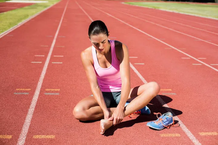 Female athlete with foot pain on running track on a sunny day