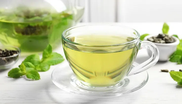 Cup with hot aromatic mint tea and fresh leaves on table