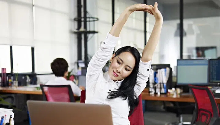 asian businesswoman looking at work on laptop computer with satisfaction and stretching arms in the air.