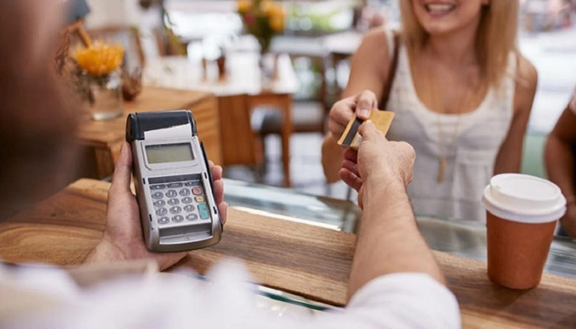 48554325 - customer paying for their order with a credit card in a cafe. bartender holding a credit card reader machine and returning the debit card to female customer after payments.