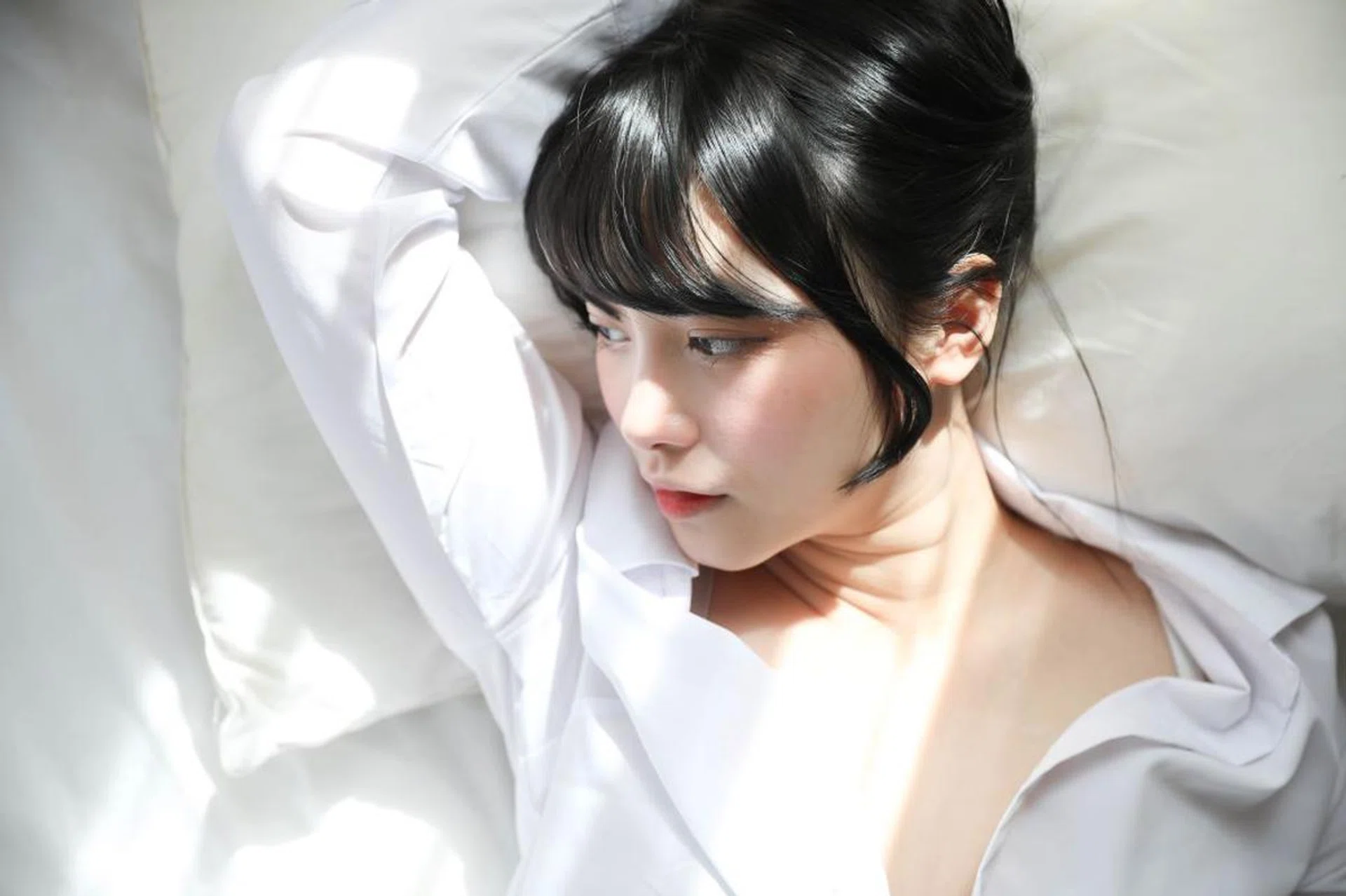 Asian girl lies on white bed, thinking