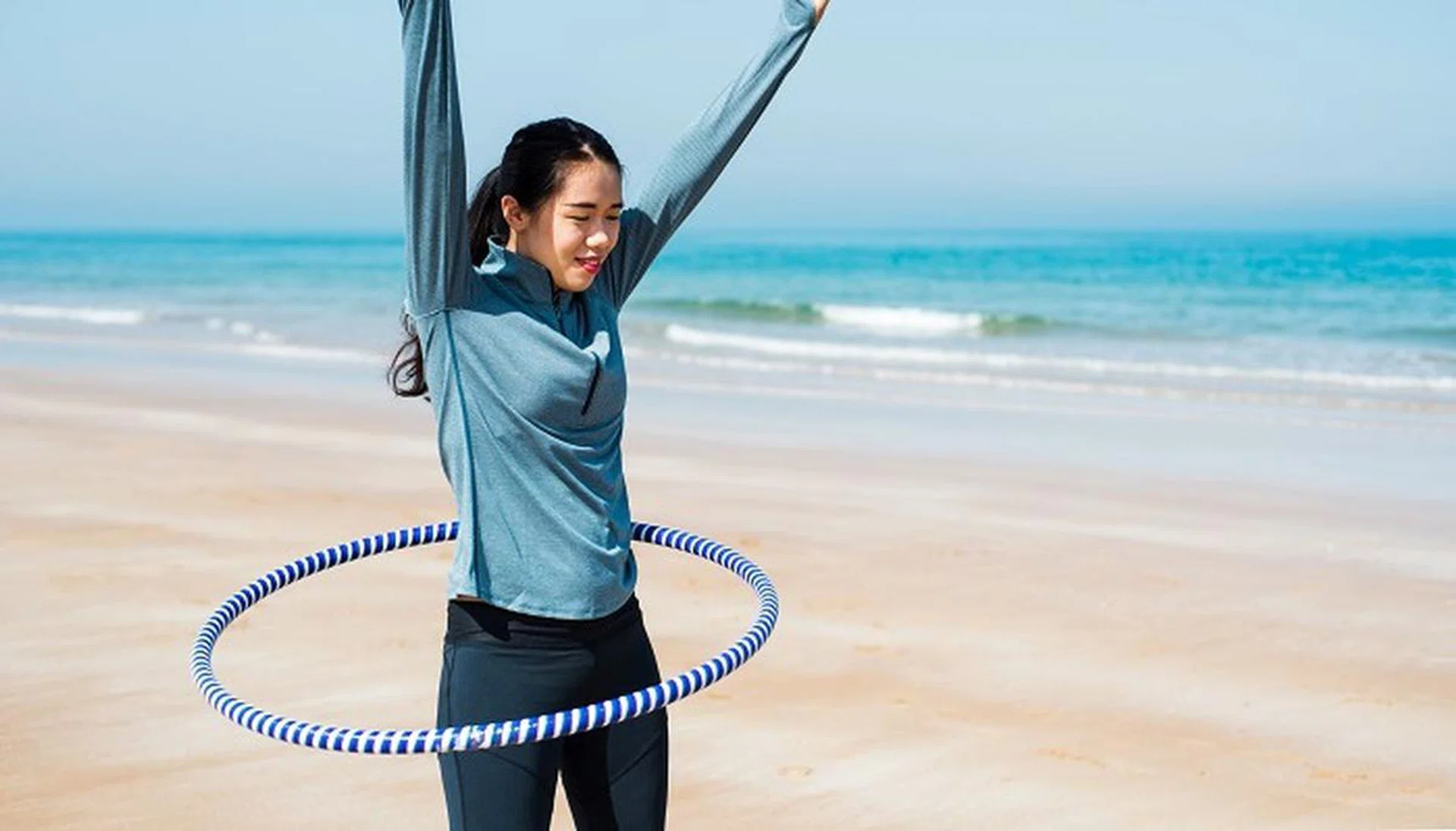 Happy woman exercising with hula hoop on the beach