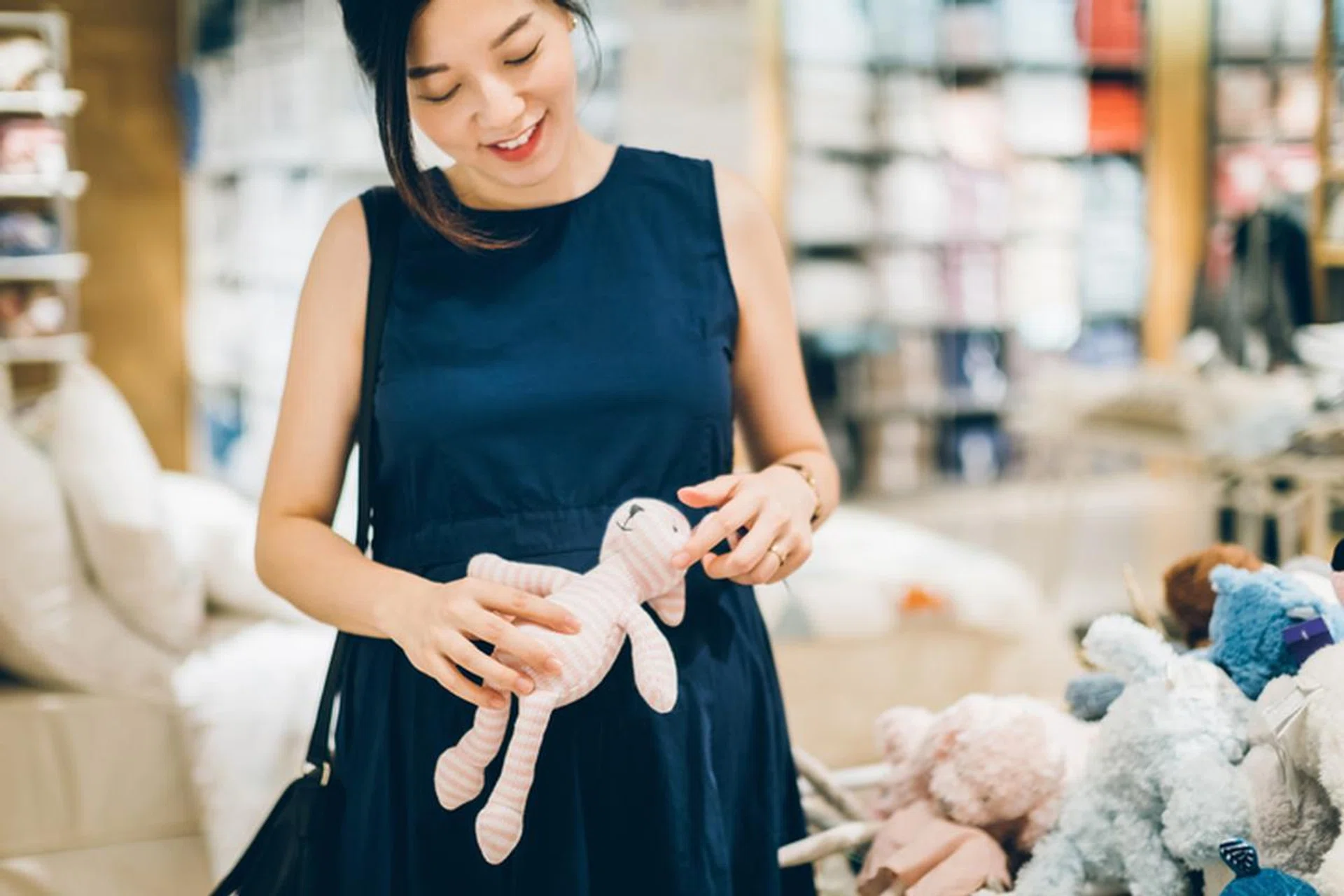 Smiling young pregnant woman shopping for baby soft toys in shop