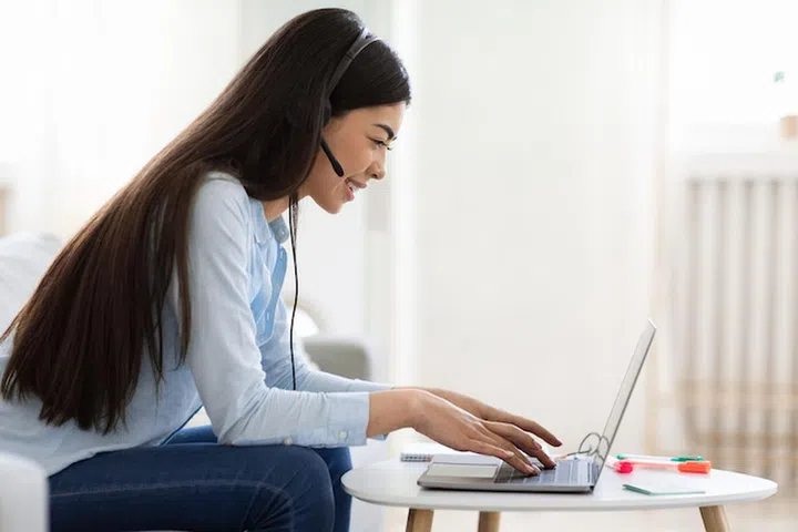 Remote Jobs For Students. Young Asian Lady Working As Call Center Operator At Home, Using Laptop And Headset, Side View
