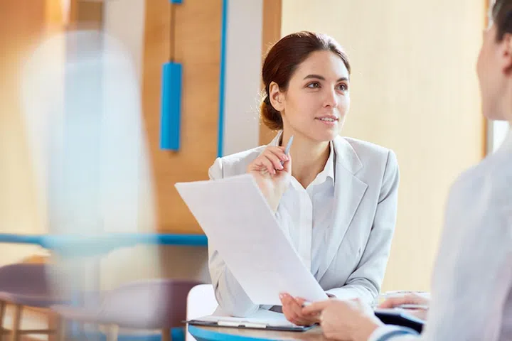 Young confident lawyer with paper consulting her client or discussing document with colleague at meeting