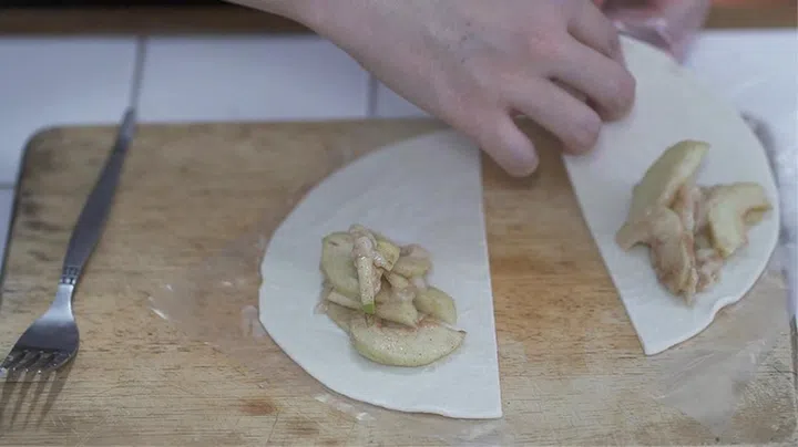 05. Cut frozen prata in half, as shown. Top with a big spoonful of apple filling. Fold pastry over and seal the edges by pressing with a fork.
05.