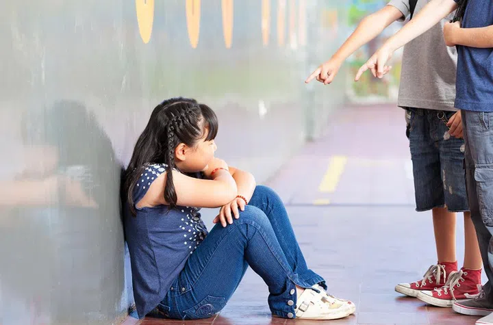 Sad pupil being bullied by classmates at corridor in school.
